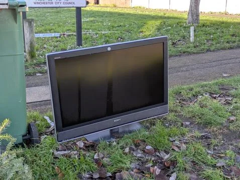 Discarded Flat Screen Television Dumped on Grass Verge Next to Public Trash B Stock Photos