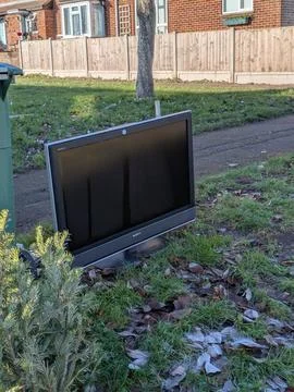 Discarded Flat Screen Television Dumped on Grass Verge Next to Public Trash B Stock Photos