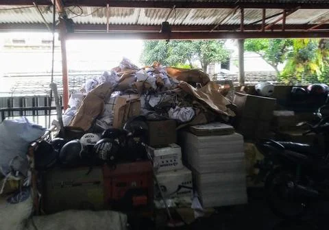 Discarded items are piled high under a corrugated metal roof in a dim, clutte Stock Photos