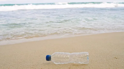 Discarded plastic bottle lies on sandy beach with waves crashing nearby Stock Footage 265162234