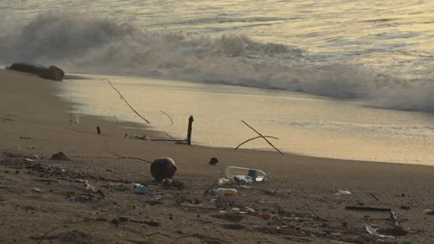 Discarded plastic bottle lying on the shore as ocean waves crash. 库存影片 331488210