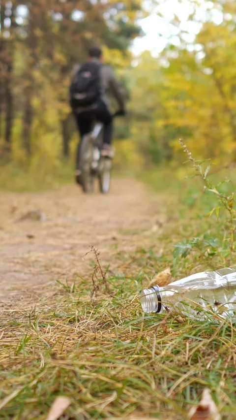 Discarded plastic bottle polluting an autumn forest path while a cyclist rides Stock Footage 347185666