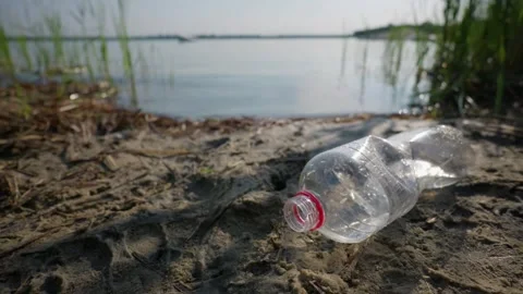 Discarded Plastic Bottle Polluting Sandy Shoreline Near Lake Water Video stock 343573140