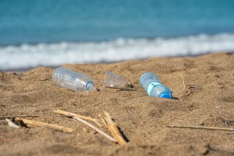 Discarded plastic bottles and cup littering the beach near the shoreline Stock Photos