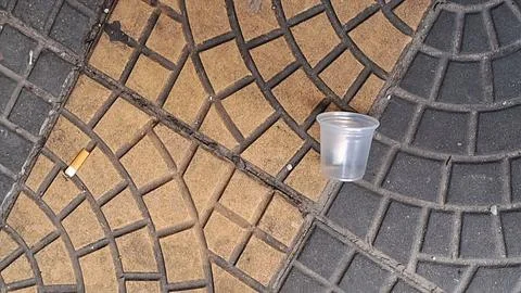 Discarded plastic cup and cigarette butt sitting on textured outdoor pavement Stock Photos