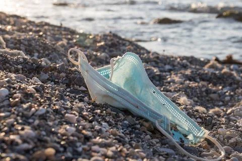 Discarded single -use face mask. Medical face mask on a beach. Stock Photos