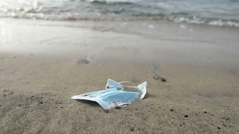 Discarded surgical face mask floating on sea shore,covid19 pandemic pollution Stock Footage 142679791