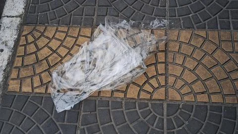 Discarded thin plastic bag lying on textured outdoor street pavement Stock Photos