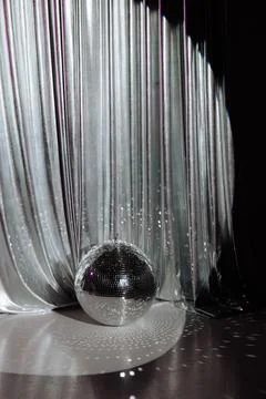 Disco ball casting light, silvery curtain backdrop. Stock Photos