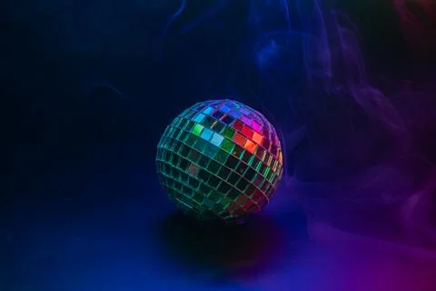 Disco ball on dark surface, reflecting colorful lights and soft smoke effects Stock Photos