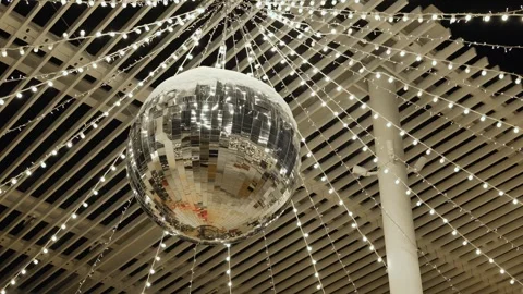 Disco ball hanging from illuminated ceiling with sparkling string lights at Stock Footage 337062209