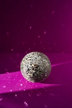 Disco ball made of irregular mirror shards on fuchsia paper background with.. Foto stock