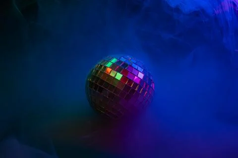Disco ball with multicolored lights and blue smoke against a party backdrop.. Stock Photos