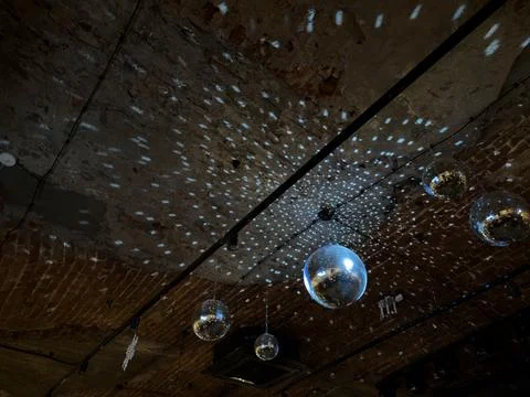 Disco ball spins on ceiling, illuminating dark space with its rays. Dance bac Stock Photos