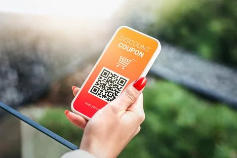 Discount coupon with QR code on smartphone in a female hand on a green grass Stock Photos