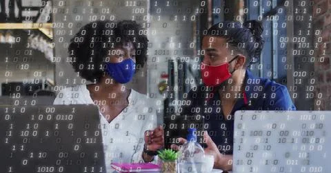 Discussing project two masked colleagues using laptops in cafe, with succulent Stock Photos