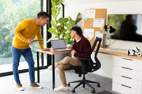 Discussing work, two men collaborating with laptop in modern home office 스톡 사진