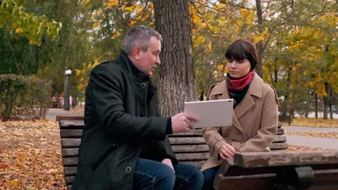 Discussion of plan for company between man and woman sitting on bench in park Stock Footage 254461920