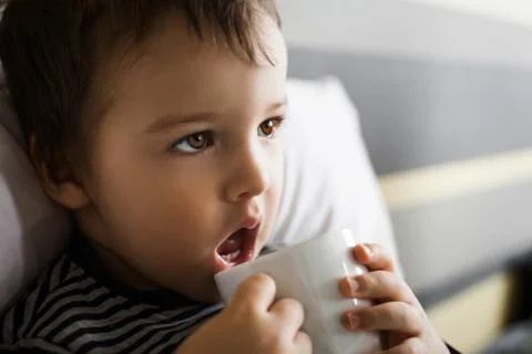 Diseased small boy drinking cup of medicament lying on bed Stock Photos