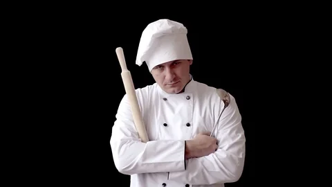 Disgruntled angry chef with rolling pin in white kitchen suit on black wall Vidéo 97863115