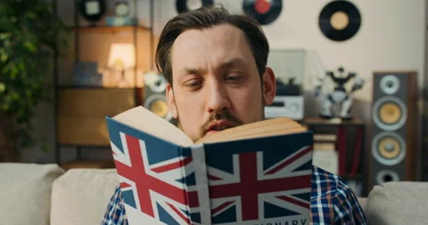 A disgruntled man with a book in hands. The old student sits on the couch Stockbeeldmateriaal 200830697