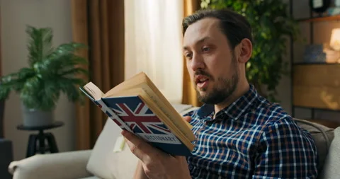 A disgruntled man with a book in hands. The old student sits on the couch Stock Footage 200831034