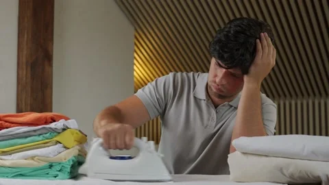 Disgruntled man with a stack of laundry and an iron. Man dissatisfied with the Stock Footage 159075476
