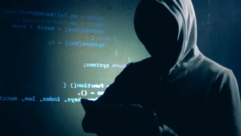 Disguised hacker is operating a tablet next to a wall with projected data Stock Footage 104208818