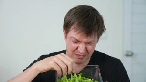Disgusted man sitting and trying to eat salad but spitting it out showing Stock Footage 314818705