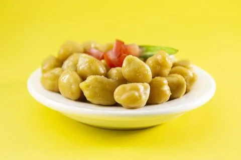 A dish of cooked chickpeas or garbanzo with tomato and green chili on yellow  Stock Photos
