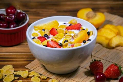 Dish with corn flakes, strawberry, cherry, peach and yogurt on the table. Stock Photos