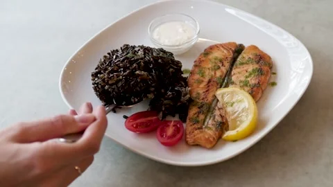 Dish with fish and black rice on a white plate. woman eating fish dinner in a Видео 139333633