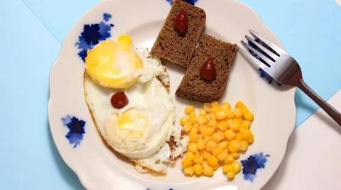 A dish with fried egg, corn and bread on a plate, where all the ingredients g Stock Photos