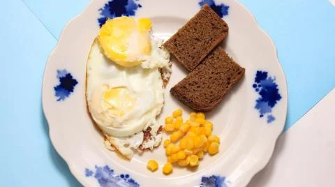 A dish with fried egg, corn and bread on a plate, where all the ingredients g Stock Photos