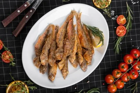 A dish of fried red mullet. Table setting, decorated with greens and cherry t Stock Photos