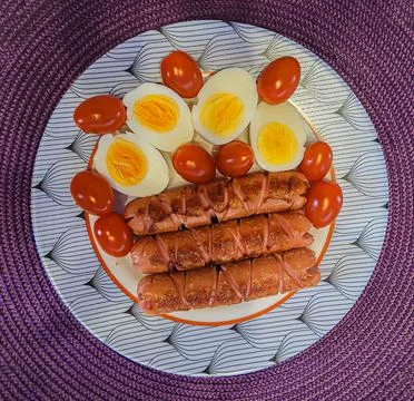 Dish with fried sausages, cherry tomatoes and cut eggs Stock Photos
