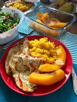 Dish includes turmeric rice, a vegetable omelette, and a fresh salad. Baked p Stock Photos
