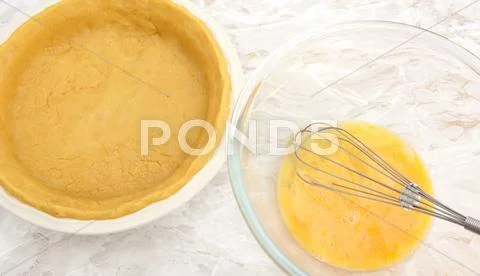 Dish lined with pastry next to bowl of beaten eggs Stock Photos