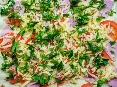 A dish prepared for baking with slices of ham tomatoes grated cheese and chopped Stock Photos