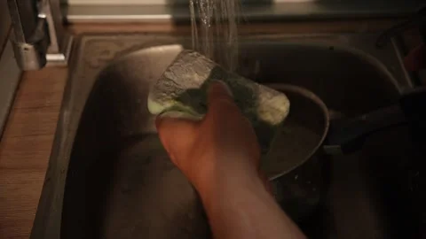 Dish soap squeezed onto sponge under running tap in sink Stock Footage 312343734