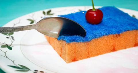A dish sponge is placed on a plate in the form of a cake with a real cherry o Stock Photos