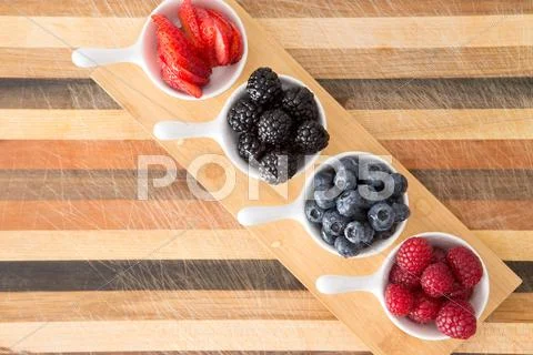 Dishes of fresh berries on decorative striped wood Stock Photos