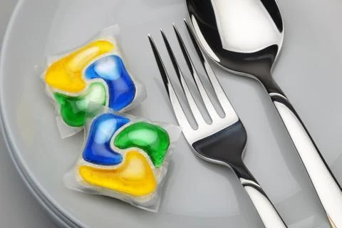 Dishwasher detergent tablet, fork and spoon Stock Photos