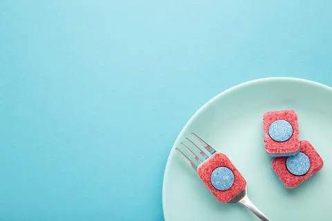 Dishwasher detergent tablet with fork and dishes on blue background. Top view Stock Photos