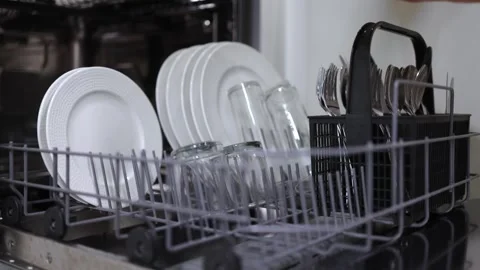 Dishwasher loading process with clean plates, glasses, and utensils arranged in Stock Footage 324307488