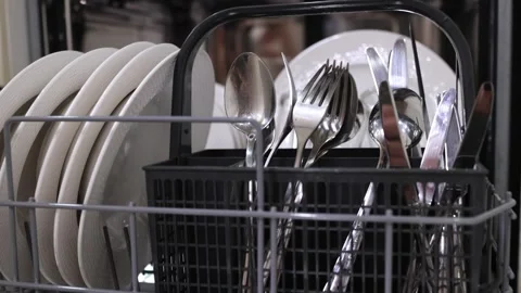 Dishwasher loading process with plates and cutlery in a basket, showing a hand Stock Footage 324307180