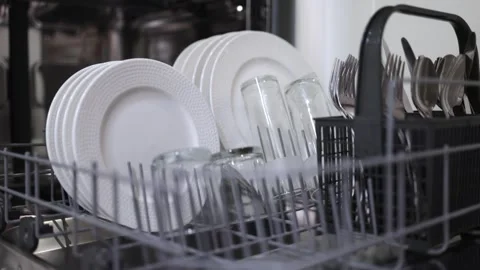 Dishwasher loading process with white plates, glasses, and cutlery arranged in Stock Footage 324295510