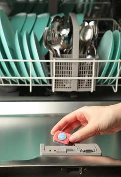 Dishwasher tablet in hand on the background of an open dishwasher. Top view Stock Photos