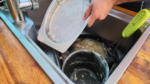 Dishwashing with sponge and detergent beside dirty dishes and cookware in a Stock Footage 345470202