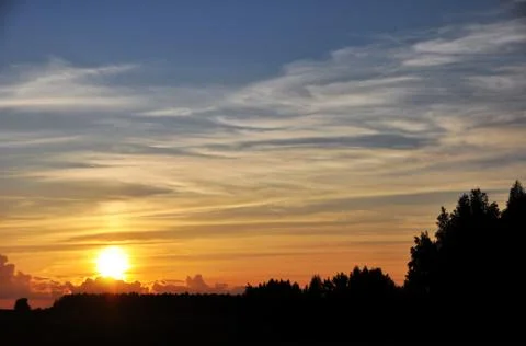 The disk of the sun sets in a translucent network of cirrus clouds at sunset. Stock Photos
